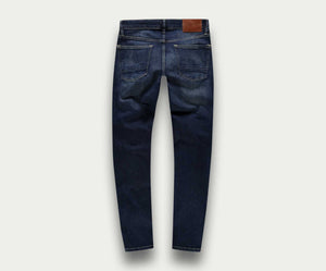 Een paar "The N01 Slim Dark Indigo Used" jeans van Blue Rivet Jeans, van achteren gezien, met twee grote zakken en een bruine leren patch op de tailleband. De denimstof heeft een licht versleten look, met subtiele vervaging en kreukels.