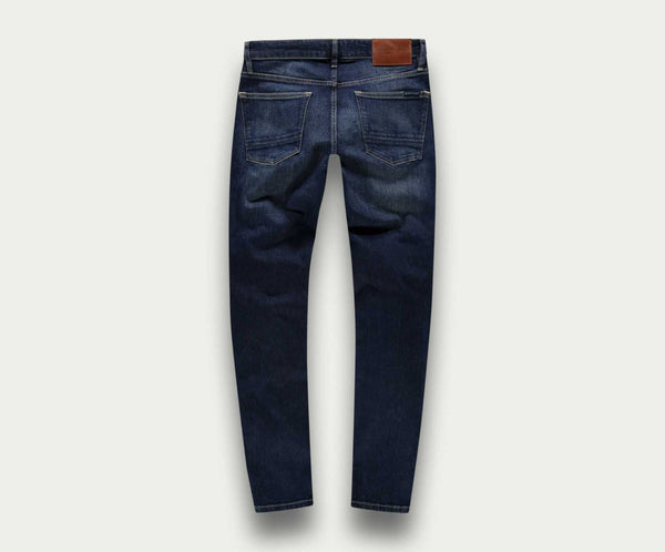 Een paar "The N01 Slim Dark Indigo Used" jeans van Blue Rivet Jeans, van achteren gezien, met twee grote zakken en een bruine leren patch op de tailleband. De denimstof heeft een licht versleten look, met subtiele vervaging en kreukels.