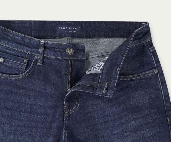 Een close-up van een paar The N01 Straight Indigo Used jeans met de rits gedeeltelijk open, waardoor de binnenstof zichtbaar is. Deze straight fit jeans van Blue Rivet Jeans hebben een knoopsluiting en zichtbare stiksels. Een label aan de binnenkant vermeldt Blue Rivet, Natural, Simple, Style.