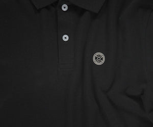 De N01 Polo Anthracite van Blue Rivet Jeans is een zwarte piqué polo, afgewerkt met grijze knopen en versierd met een cirkelvormig embleem met een abstract ontwerp op de linkerborst. Het is gemaakt van biologisch katoen voor een vleugje zomerse chic.