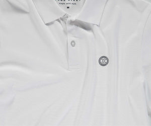 Een wit poloshirt van Blue Rivet Jeans, bekend als The N01 Polo White, met korte mouwen en een klein cirkelvormig embleem met patroon op de linkerborst. Dit shirt heeft een kraag en twee knopen. Binnenin staat op het label BLUE RIVER simple. solid. style. M.