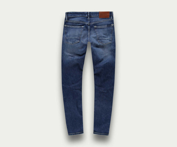 Achteraanzicht van The N01 Slim Indigo Used jeans van Blue Rivet Jeans, met vervaagde details en een bruine leren patch op de tailleband. De spijkerbroek wordt getoond tegen een lichte achtergrond.