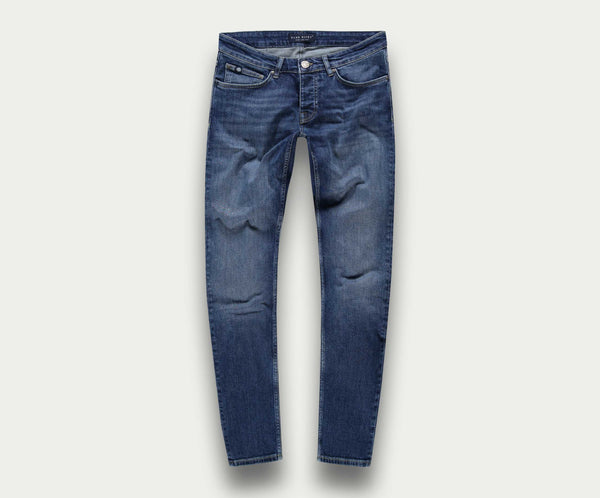De N01 Slim Indigo Used jeans van Blue Rivet Jeans worden plat tegen een lichte achtergrond getoond, waarbij het klassieke five-pocket design en subtiele dijvervaging worden getoond. Gemaakt van premium stretchstof, bieden ze ongeëvenaard comfort en stijl.