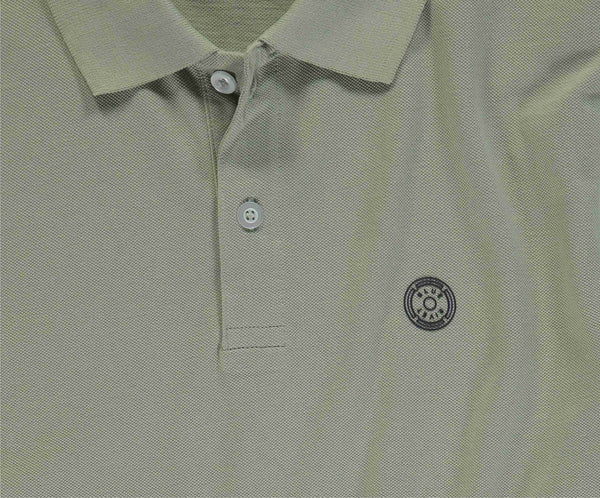 Close-up van The N01 Polo Seagrass van Blue Rivet Jeans, met een lichtgroene textuurstof en korte mouwen. Deze heren polo heeft twee knopen bij de kraag en een cirkelvormig geborduurd logo op de linkerborst.
