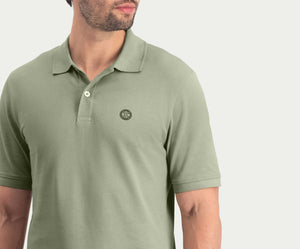 Een man draagt The N01 Polo Seagrass van Blue Rivet Jeans, met korte mouwen en een klein rond logo op de borst. De achtergrond is effen en lichtgekleurd, waarbij alleen de bovenste helft van zijn torso en een deel van zijn gezicht worden benadrukt.