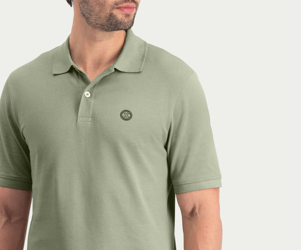 Een man draagt The N01 Polo Seagrass van Blue Rivet Jeans, met korte mouwen en een klein rond logo op de borst. De achtergrond is effen en lichtgekleurd, waarbij alleen de bovenste helft van zijn torso en een deel van zijn gezicht worden benadrukt.