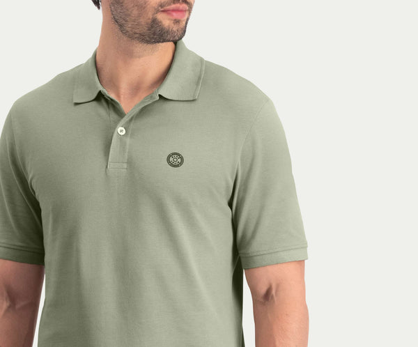 Een man draagt The N01 Polo Seagrass van Blue Rivet Jeans, met korte mouwen en een klein rond logo op de linkerborst. De afbeelding is bijgesneden op de schouders en taille, met de nadruk op de details van het shirt.