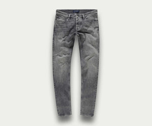 De N01 Slim Light Grey Used van Blue Rivet Jeans worden getoond tegen een eenvoudige, lichte achtergrond. Deze stretchjeans hebben een klassiek five-pocket-ontwerp met een slim fit, compleet met subtiele kreukels op de dijen voor een natuurlijk ingedragen uiterlijk.