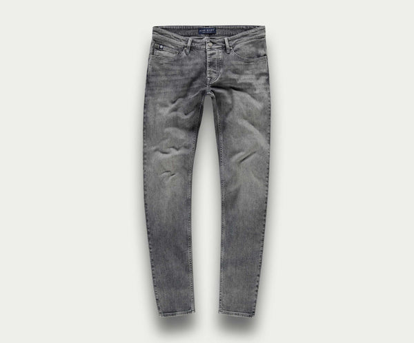 De N01 Slim Light Grey Used van Blue Rivet Jeans worden getoond tegen een eenvoudige, lichte achtergrond. Deze stretchjeans hebben een klassiek five-pocket-ontwerp met een slim fit, compleet met subtiele kreukels op de dijen voor een natuurlijk ingedragen uiterlijk.