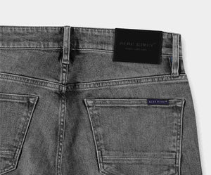Een close-up van de achterkant van The N01 Slim Light Grey Used jeans benadrukt twee achterzakken en een zwarte leren patch op de tailleband. Een klein label met de merknaam Blue Rivet Jeans is zichtbaar boven de rechterzak, wat het stretchcomfort en de moderne stijl benadrukt.