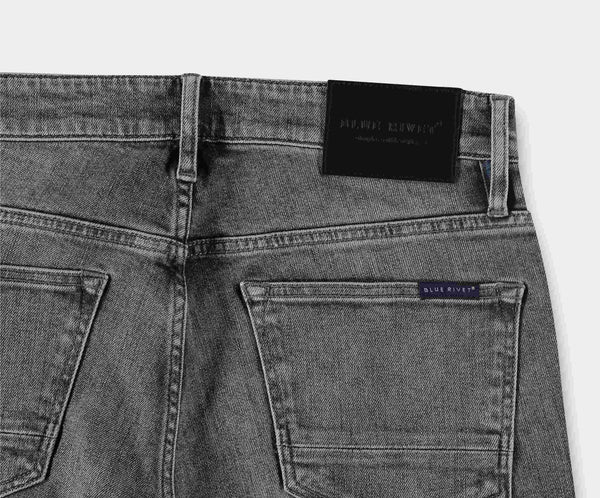 Een close-up van de achterkant van The N01 Slim Light Grey Used jeans benadrukt twee achterzakken en een zwarte leren patch op de tailleband. Een klein label met de merknaam Blue Rivet Jeans is zichtbaar boven de rechterzak, wat het stretchcomfort en de moderne stijl benadrukt.