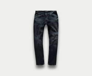 Een paar "The N01 Slim Blue Black Used" jeans van Blue Rivet Jeans wordt getoond op een lichtgrijze achtergrond. Deze spijkerbroek heeft subtiele vervagings- en kreukdetails met standaardzakken en riemlussen, wat zorgt voor een klassieke en veelzijdige uitstraling.