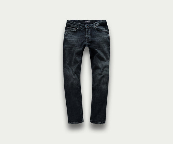 Een paar "The N01 Slim Blue Black Used" jeans van Blue Rivet Jeans wordt getoond op een lichtgrijze achtergrond. Deze spijkerbroek heeft subtiele vervagings- en kreukdetails met standaardzakken en riemlussen, wat zorgt voor een klassieke en veelzijdige uitstraling.