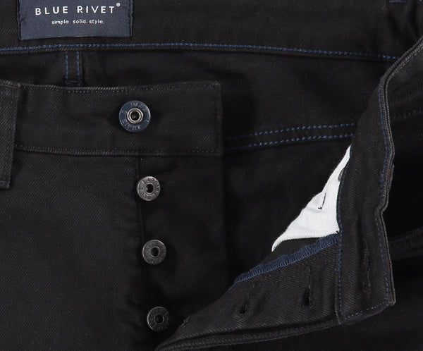 Close-up van The N01 Slim Black premium denim jeans, met een zichtbare knoopsluiting en blauwe stiksels. Het Blue Rivet Jeans merklabel is in de tailleband genaaid, wat de kwaliteit van deze spijkerbroek benadrukt.