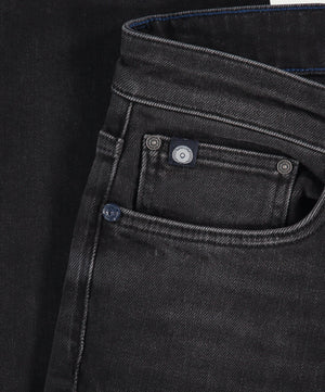 Close-up van Blue Rivet Jeans' The N01 Slim Black Used denim, met de nadruk op de voorzak en taille. De premium stof heeft een lichte glans met zichtbare randstiksels, geaccentueerd door twee metalen klinknagels bij de zak.