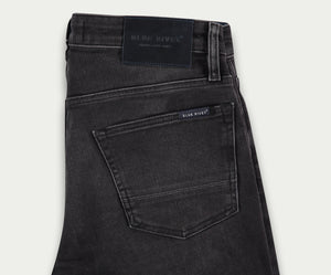 Close-up van de N01 Slim Black Used jeans van Blue Rivet Jeans, met een zichtbare achterzak en een label op de tailleband met de merknaam. De zak bevat een klein label met dezelfde branding. De stretchstof heeft een licht vervaagde textuur, wat de chique uitstraling versterkt.