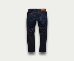Een paar The N01 Slim Dark Indigo jeans van Blue Rivet Jeans, met een donkerblauw denimontwerp met twee achterzakken en een bruine leren patch op de tailleband, wordt van achteren afgebeeld op een effen lichtgrijze achtergrond.