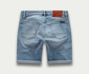 Achteraanzicht van The N01 Short Stone Bleached in lichtblauwe denim, met opgerolde zomen, twee achterzakken en een bruine leren patch op de tailleband. Het merk Blue Rivet Jeans is te zien op de patch, wat de klassieke denimcharme benadrukt.