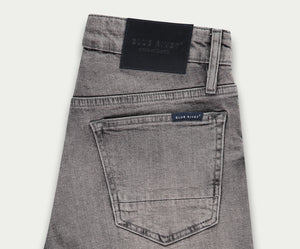 Een paar lichtgrijze jeans netjes opgevouwen, met een achterzak met een klein label met de tekst Blue Rivet Jeans. Een zwarte leren patch siert de tailleband, wat een vleugje elegantie toevoegt aan deze veelzijdige denim essentials die bekend staan als The N01 Short Light Grey Used.