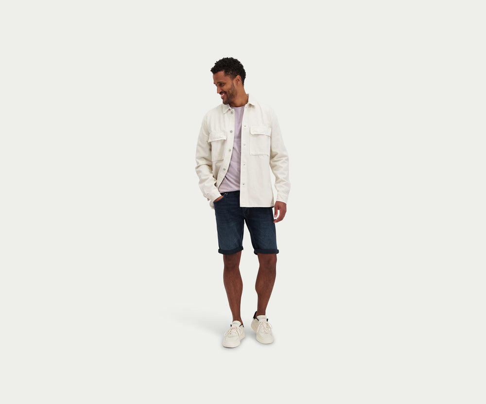 Een persoon die The N01 Short Blue Black van Blue Rivet Jeans draagt en witte sneakers staat tegen een effen witte achtergrond. Alleen de onderkant van het lichaam is zichtbaar.