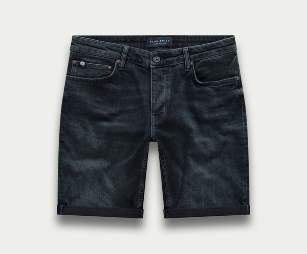 De N01 Short Blue Black van Blue Rivet Jeans heeft een klassiek five-pocket design, knoopsluiting en subtiele stikdetails. De zomen zijn netjes gevouwen tegen een effen lichtgrijze achtergrond.