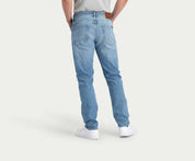 Een persoon is van achteren te zien met de N01 Straight Stone Bleached jeans van Blue Rivet Jeans en witte sneakers. De lichtblauwe denim jeans heeft zichtbare achterzakken en een bruine leren patch op de tailleband, allemaal tegen een effen witte achtergrond.