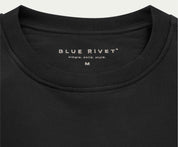 Close-up van een zwart T-shirt met het label Blue Rivet Jeans boven hun slogan simple. solid. style., met maat M op de binnenkant van de kraag. Gemaakt van biologisch katoen, dit zachte en nauwsluitende stuk is gemaakt voor degenen die premium kwaliteit waarderen, verwant aan onze geliefde The N01 Sweat Anthracite-lijn.