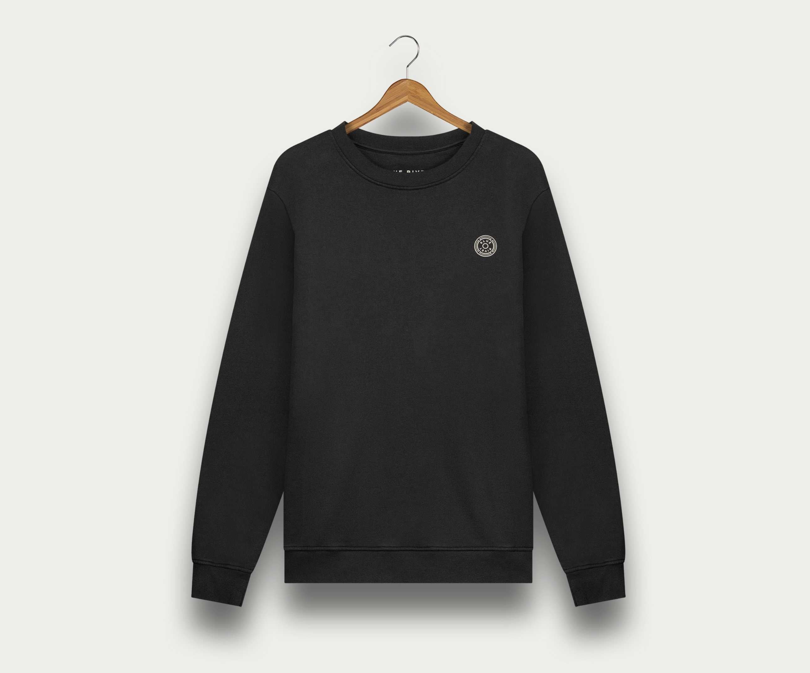 De N01 Sweat Anthracite van Blue Rivet Jeans is een zwarte crewneck sweater van biologisch katoen, afgebeeld op een houten hanger tegen een lichte achtergrond. Deze premium sweater voor heren heeft een klein rond logo op de linkerborst.