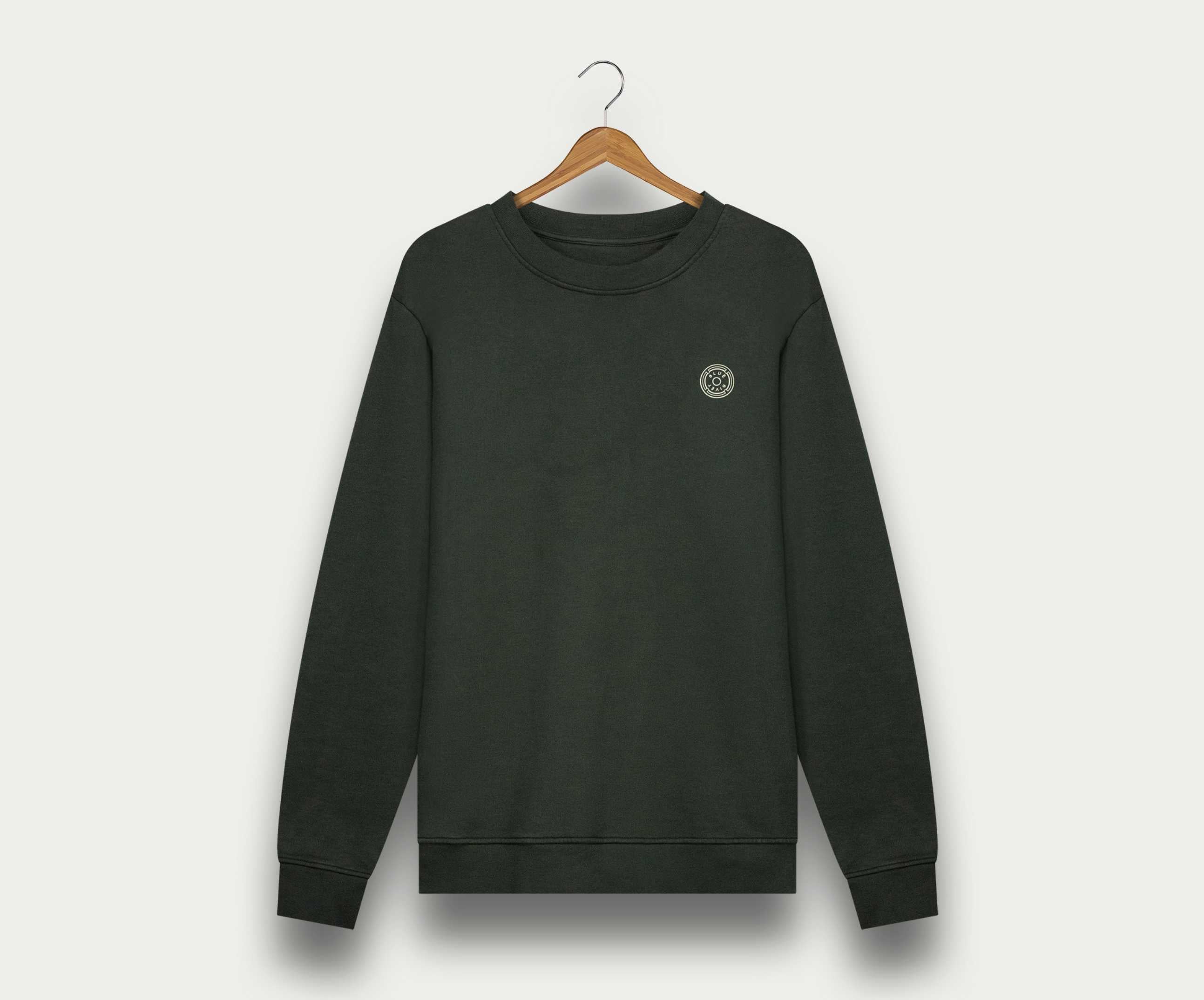 De N01 Sweat Dark Green van Blue Rivet Jeans, een effen donkergroene herentrui van biologisch katoen, met een klein rond logo op de borst, hangt elegant op een houten hanger tegen een witte achtergrond.