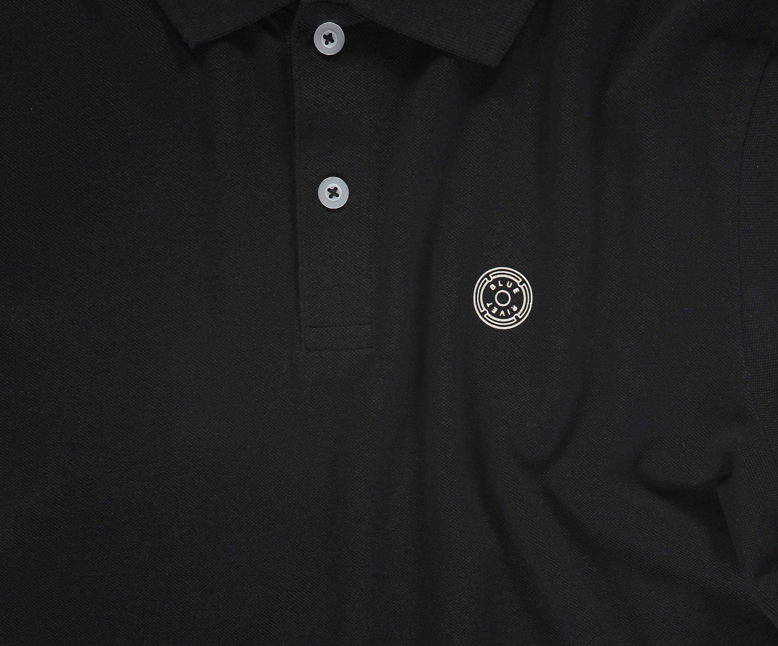 De N01 Polo Anthracite van Blue Rivet Jeans is een zwarte piqué polo, afgewerkt met grijze knopen en versierd met een cirkelvormig embleem met een abstract ontwerp op de linkerborst. Het is gemaakt van biologisch katoen voor een vleugje zomerse chic.