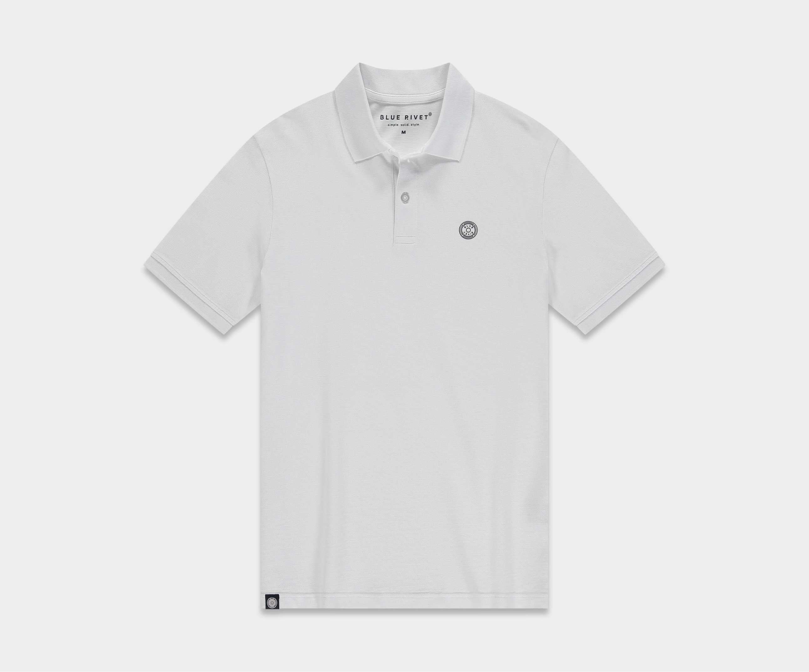 De N01 Polo White van Blue Rivet Jeans is een effen witte heren polo met korte mouwen en een klein geborduurd logo op de linkerborst. Het heeft een klassieke kraag en een sluiting met drie knopen, plat gelegd tegen een neutrale achtergrond.