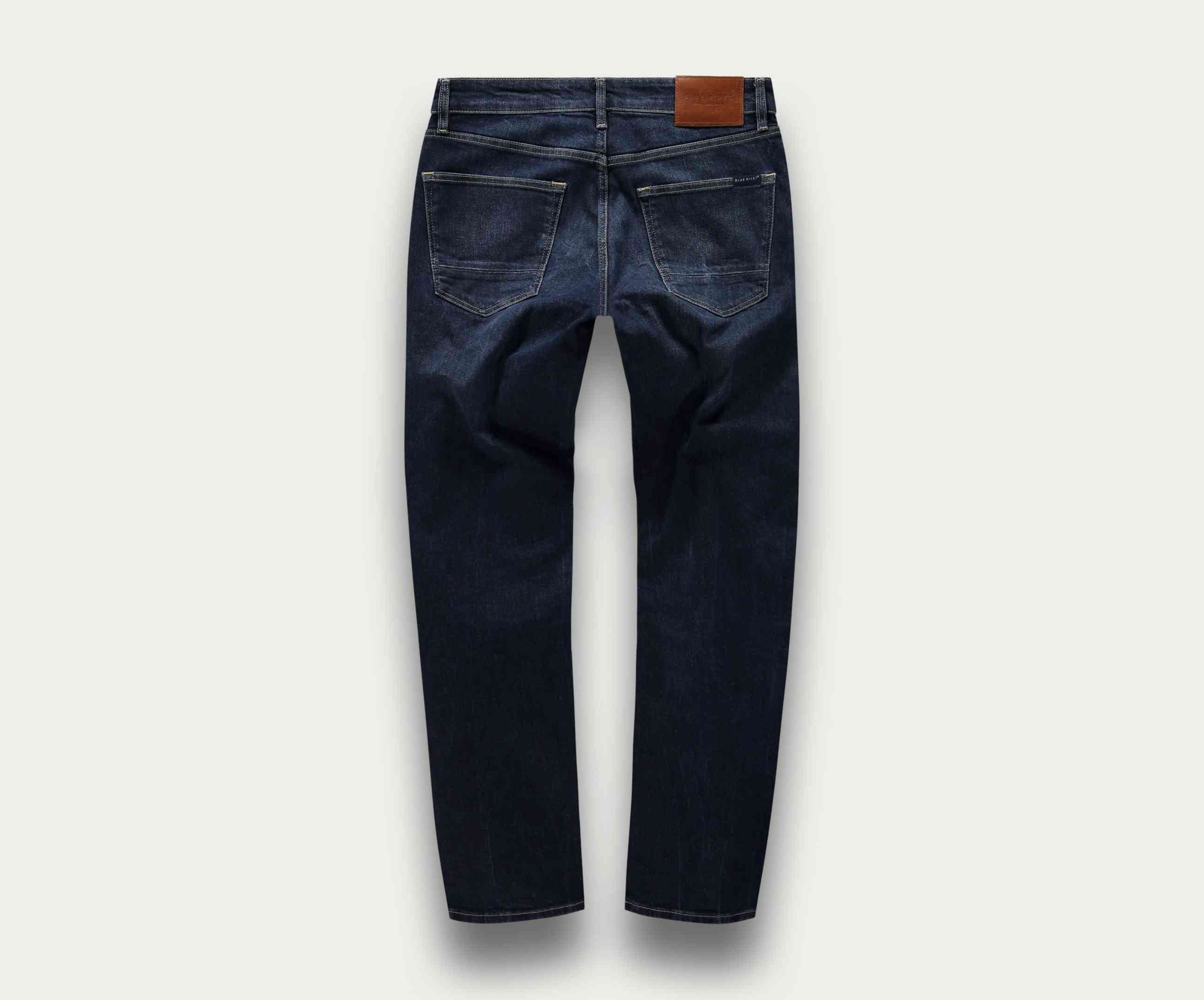 De afbeelding toont de N01 Straight Dark Indigo Used jeans van Blue Rivet Jeans, met een klassieke straight-leg stijl in een donkere indigo tint. Van achteren gezien, benadrukken deze jeans gestikte zakken, zichtbare naden en een bruine leren patch op de tailleband, wat tijdloze denimmode belichaamt.