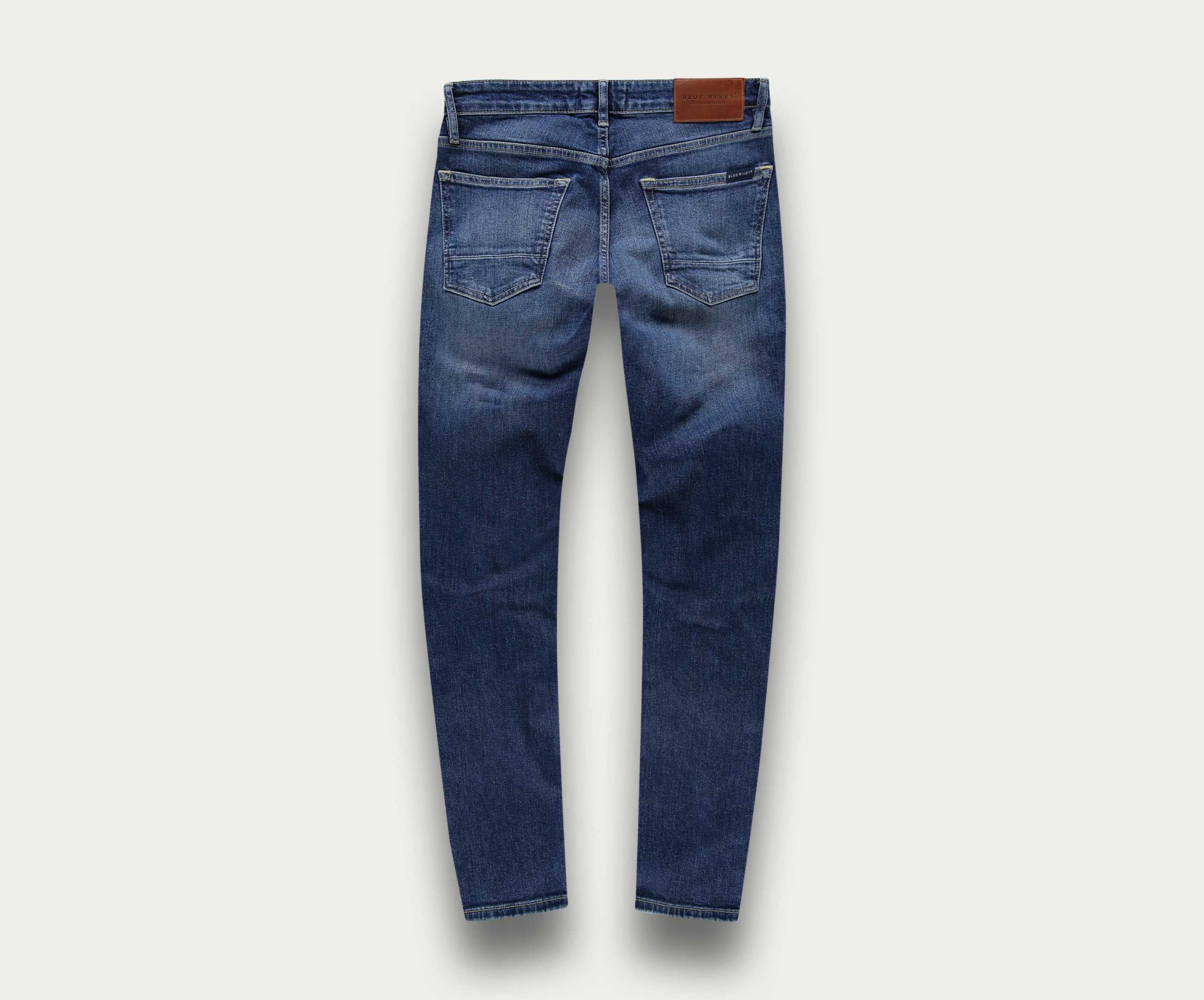 Achteraanzicht van The N01 Slim Indigo Used jeans van Blue Rivet Jeans, met vervaagde details en een bruine leren patch op de tailleband. De spijkerbroek wordt getoond tegen een lichte achtergrond.