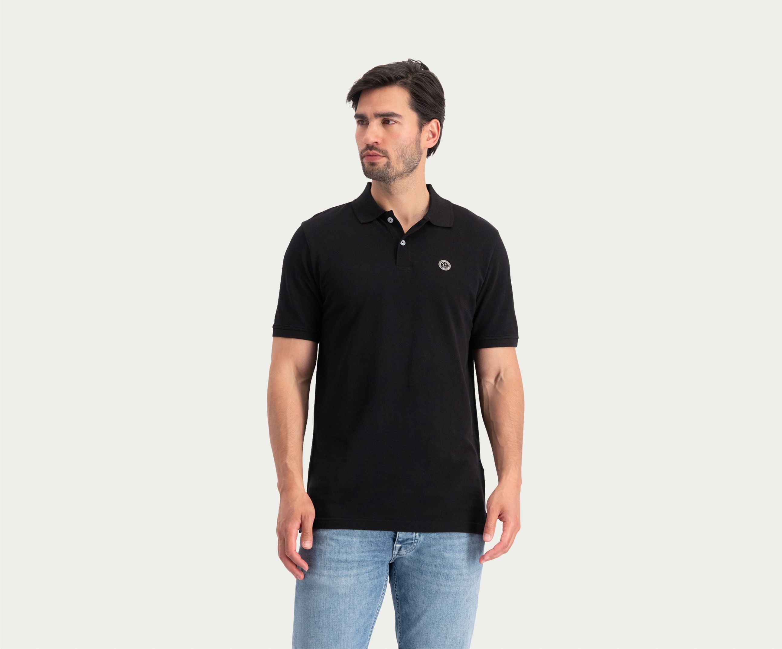 Een persoon die de N01 Polo Anthracite and Blue Rivet Jeans draagt, staat tegen een effen witte achtergrond, kijkt naar links en straalt zomerse chic uit.