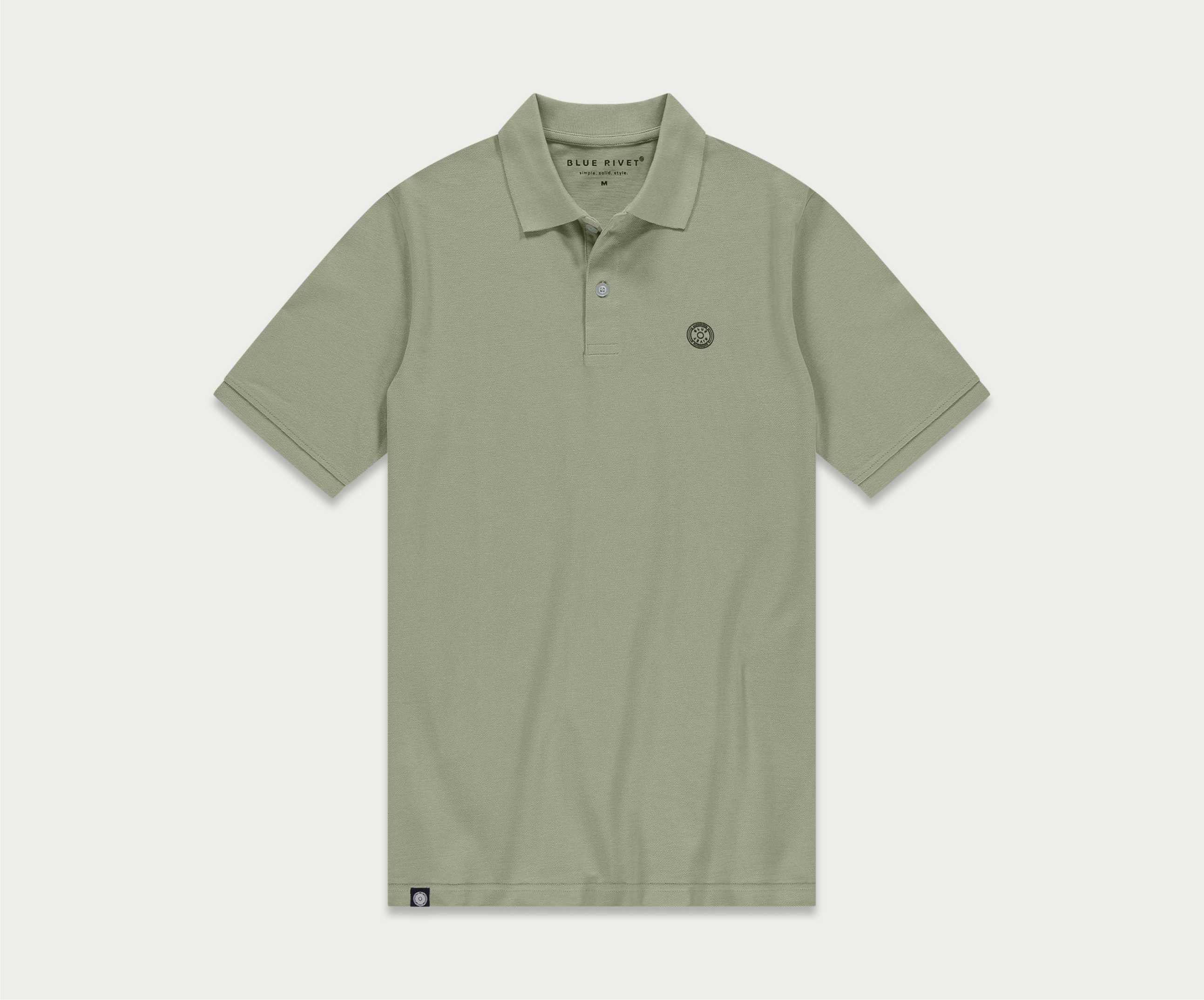 Introductie van de N01 Polo Seagrass van Blue Rivet Jeans: een lichtgroene polo met korte mouwen en een subtiel logo op de linkerborst. Dit shirt is ontworpen met een klassieke kraag en een sluiting met drie knopen, gepresenteerd tegen een effen witte achtergrond.