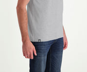 Een persoon die The N01 Tee Grey Melee and Blue Rivet Jeans in donkerblauw draagt, staat met zijn armen ontspannen langs zijn lichaam tegen een effen witte achtergrond. De casual outfit toont een klein logolabel aan de zijkant van het t-shirt.