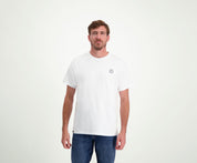 Tegen een effen lichte achtergrond straalt een man met kort bruin haar en een baard nonchalant zelfvertrouwen uit terwijl hij met zijn handen ontspannen langs zijn lichaam staat. Hij draagt The N01 Tee White van Blue Rivet Jeans, perfect gecombineerd met een blauwe jeans.