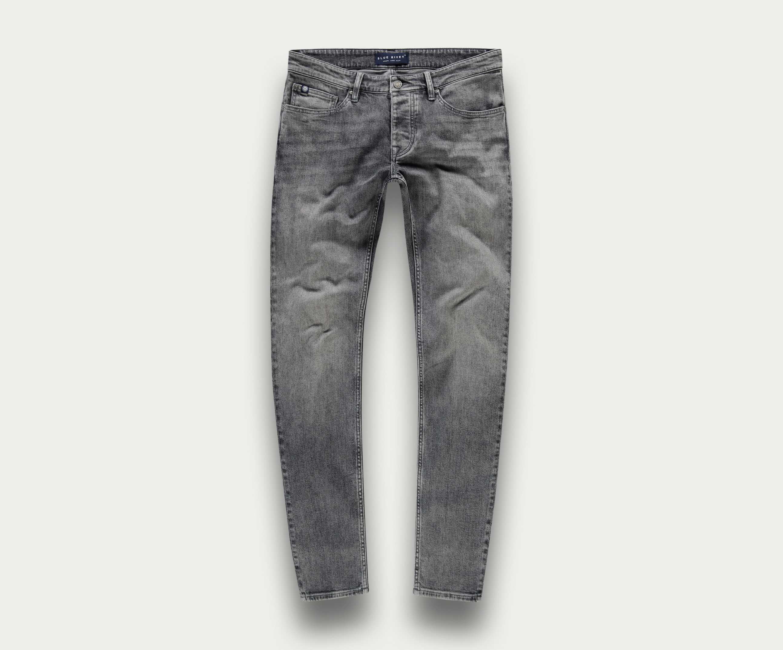 De N01 Slim Light Grey Used van Blue Rivet Jeans worden getoond tegen een eenvoudige, lichte achtergrond. Deze stretchjeans hebben een klassiek five-pocket-ontwerp met een slim fit, compleet met subtiele kreukels op de dijen voor een natuurlijk ingedragen uiterlijk.