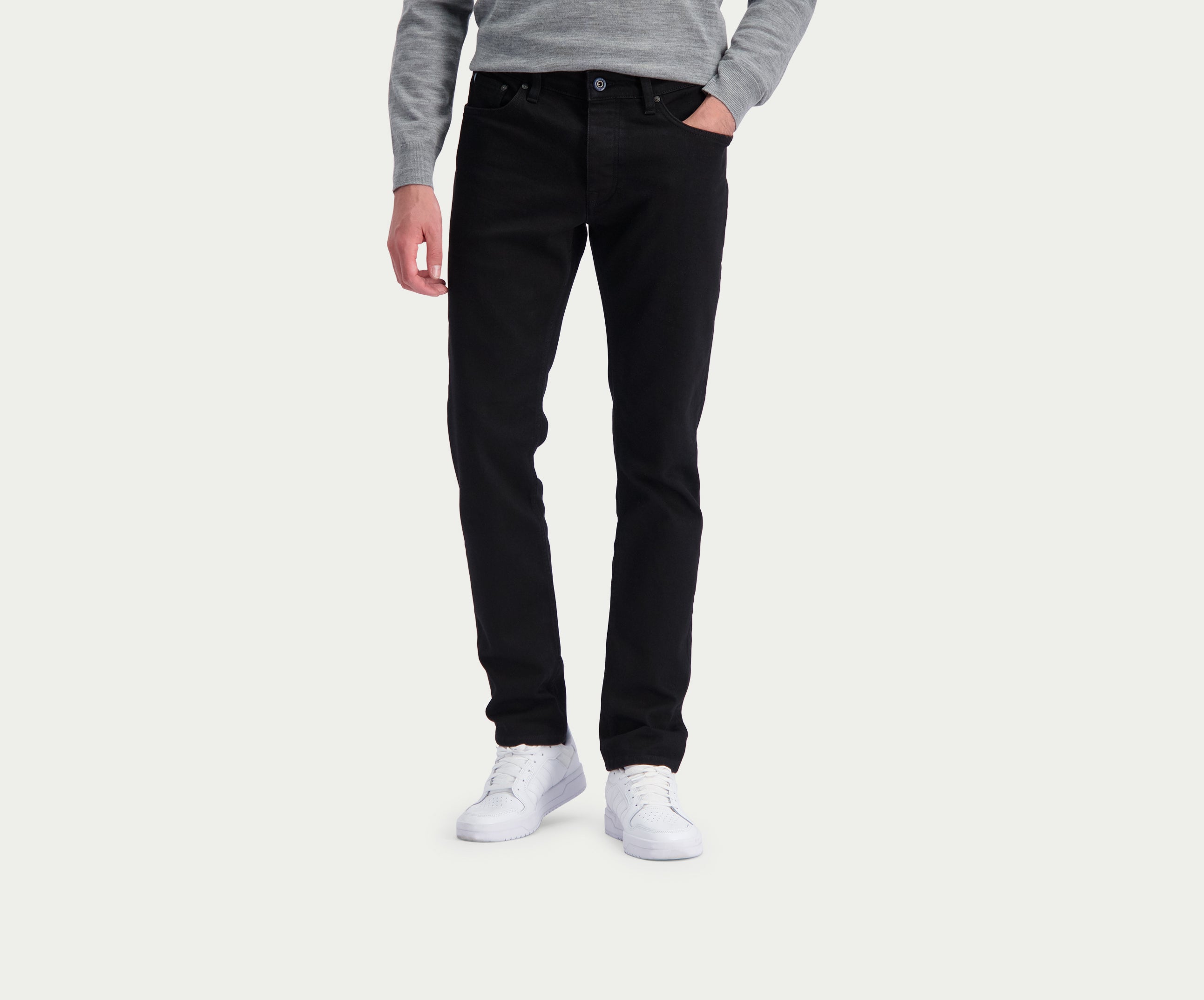 Een persoon draagt de N01 Slim Black jeans van Blue Rivet Jeans, een grijze trui en witte sneakers tegen een effen achtergrond.