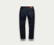 Een paar The N01 Slim Dark Indigo jeans van Blue Rivet Jeans, met een donkerblauw denimontwerp met twee achterzakken en een bruine leren patch op de tailleband, wordt van achteren afgebeeld op een effen lichtgrijze achtergrond.