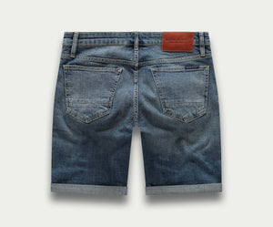 Achteraanzicht van The N01 Short Dark Indigo Vintage van Blue Rivet Jeans, of "korte broek", met opgerolde zomen. Deze shorts hebben twee achterzakken en een bruine leren patch op de tailleband. De denimstof heeft een vervaagde, versleten look.