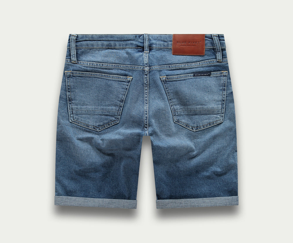 Een paar The N01 Short Indigo Used by Blue Rivet Jeans, met een klassiek five-pocket-ontwerp, knoopsluiting en gerolde manchetten, afgebeeld op een effen witte achtergrond.
