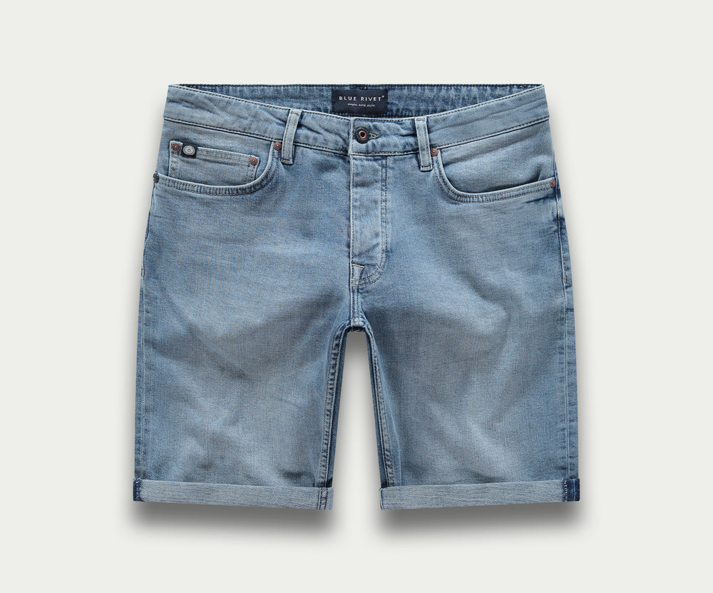 Achteraanzicht van The N01 Short Stone Bleached in lichtblauwe denim, met opgerolde zomen, twee achterzakken en een bruine leren patch op de tailleband. Het merk Blue Rivet Jeans is te zien op de patch, wat de klassieke denimcharme benadrukt.