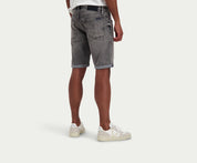 Een persoon die een wit t-shirt draagt, The N01 Short Light Grey Used by Blue Rivet Jeans in grijze denim, en off-white sneakers staat tegen een effen witte achtergrond. De afbeelding richt zich op de achterkant van de outfit, waarbij de opgerolde zoom van de shorts wordt benadrukt.