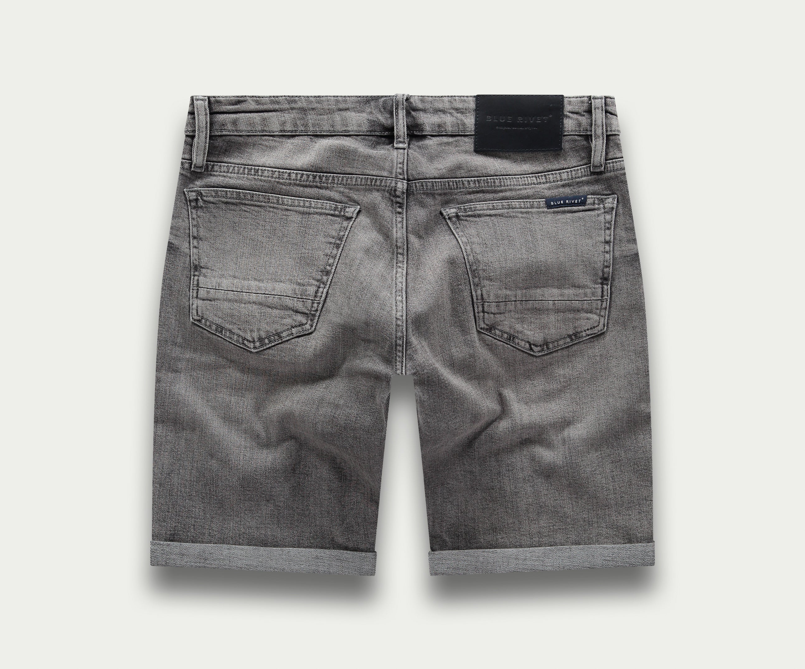 De achterkant van "The N01 Short Light Grey Used" van Blue Rivet Jeans toont een paar grijze denim shorts met opgerolde zomen. Deze shorts, ook wel "korte broek" genoemd, hebben twee achterzakken en een zwart taillebandlabel. De licht vervaagde stof versterkt hun casual, versleten uiterlijk.